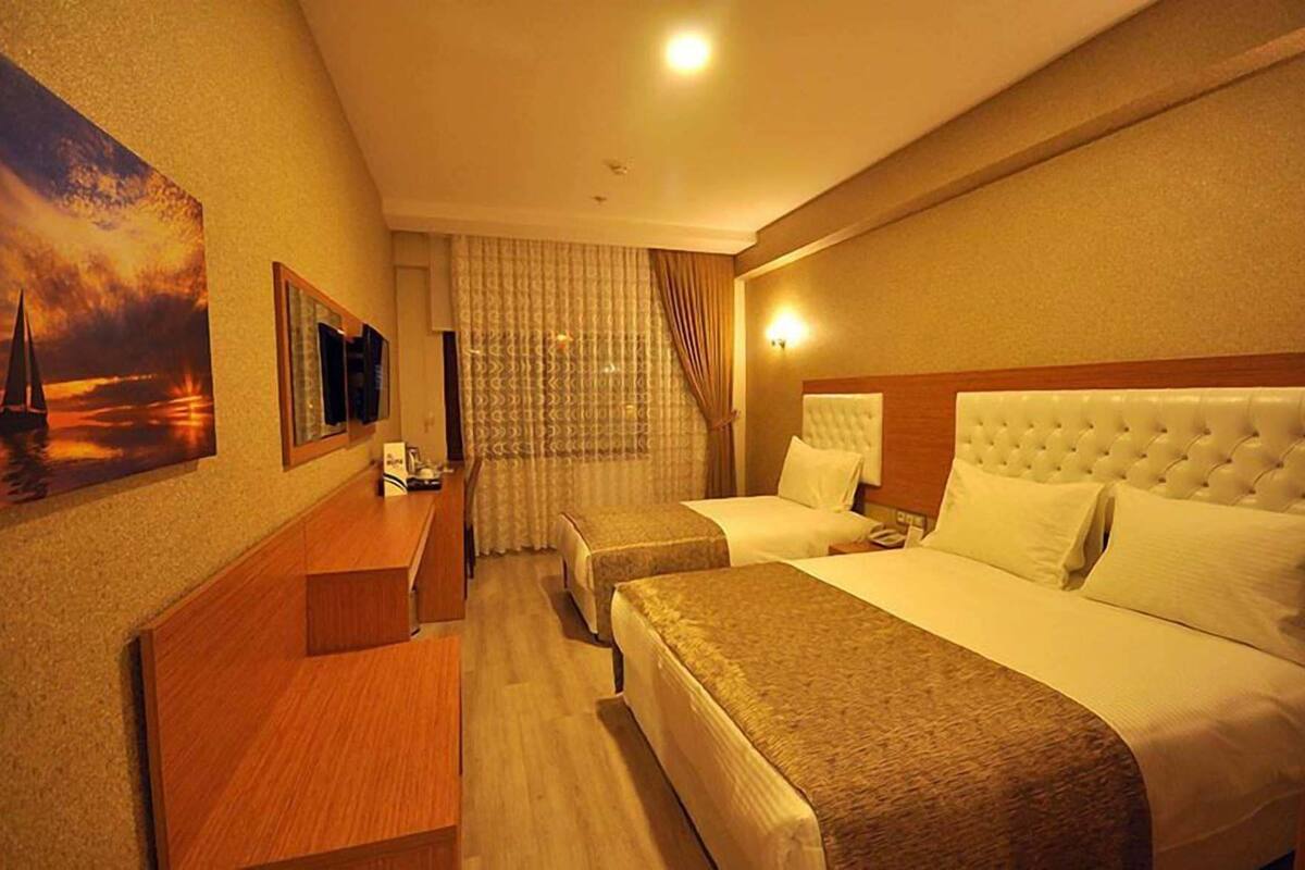A hotel room with two beds, a desk, a TV, and a painting of a sunset.