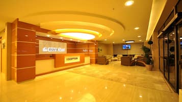 A hotel reception area with a reception desk, seating area, and a television screen.