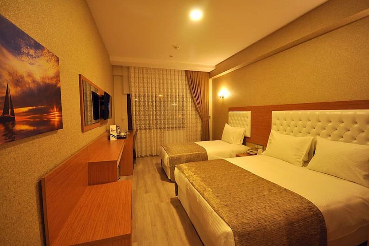 A hotel room with two beds, a wooden desk, a television, and a painting of a sunset.