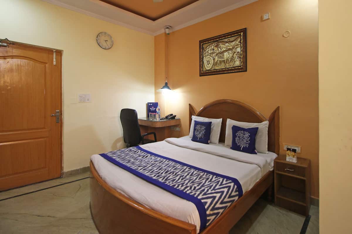 A hotel room with a bed, desk, chair, and a clock on the wall.