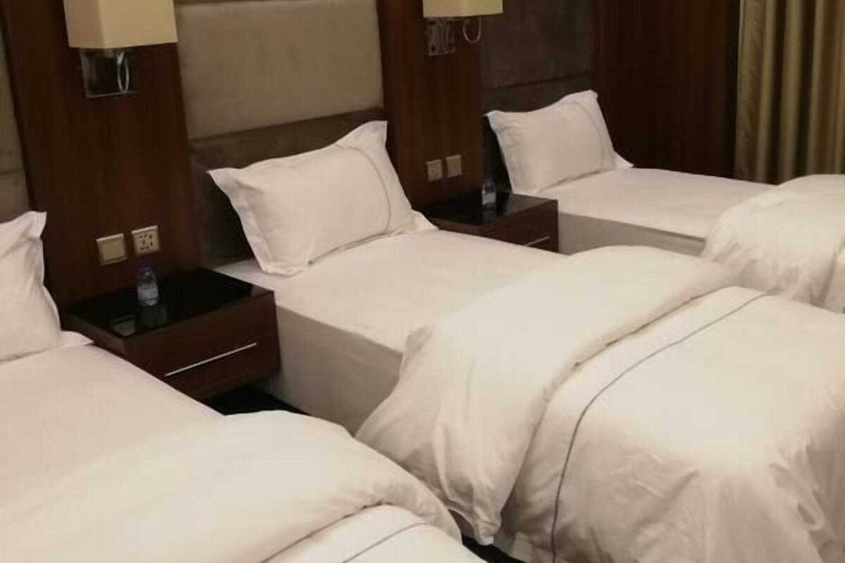 A hotel room with three single beds, each with a nightstand and a lamp.