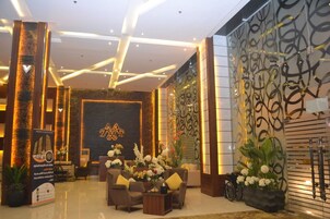 A modern hotel lobby with a reception desk, seating area, and decorative wall panels.