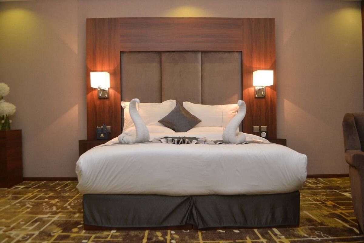 A large bed with a wooden headboard, two wall-mounted lamps, and a decorative pillow.