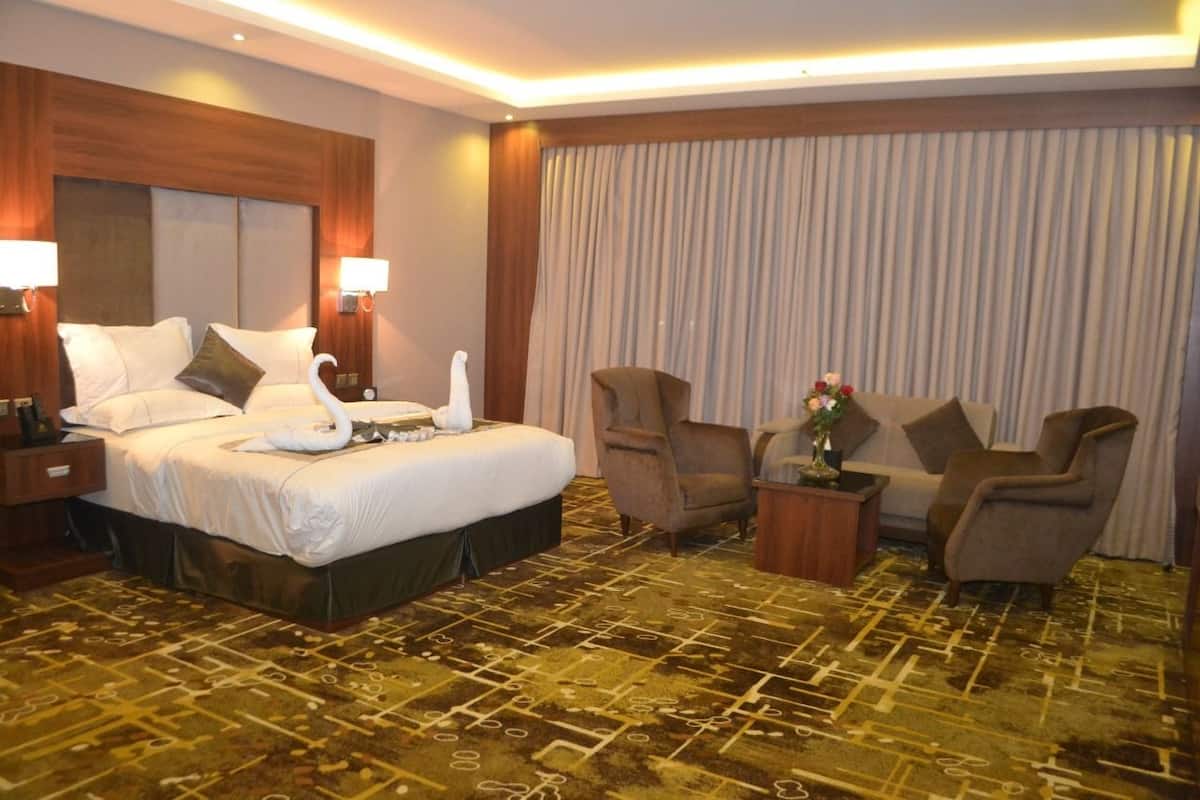 A hotel room with a large bed, two armchairs, a small table with a vase, and a curtain.