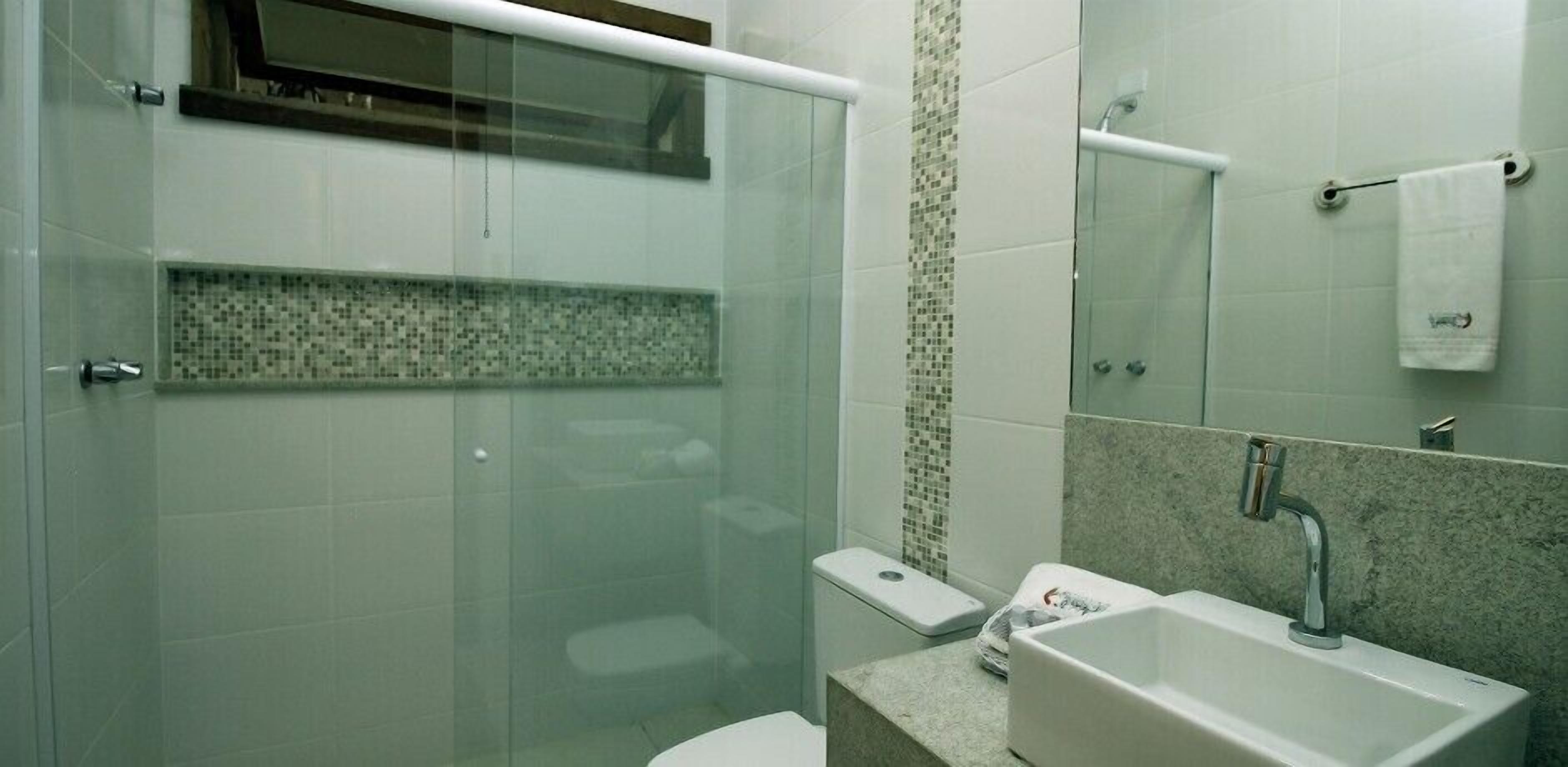 A modern bathroom with a glass shower enclosure, a toilet, a sink with a marble countertop, and a tiled backsplash.