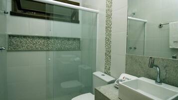 A modern bathroom with a glass shower enclosure, a toilet, a sink with a marble countertop, and a tiled backsplash.