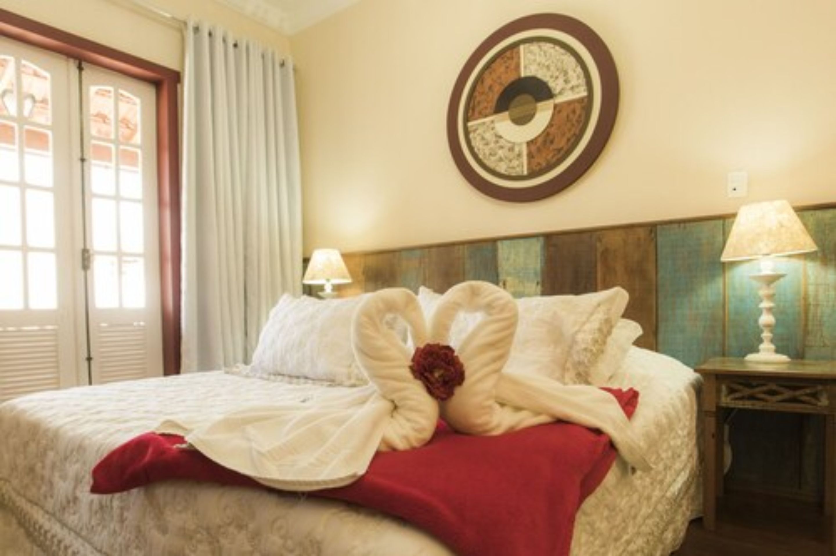 A hotel room with a bed, a wall clock, and a window with curtains.