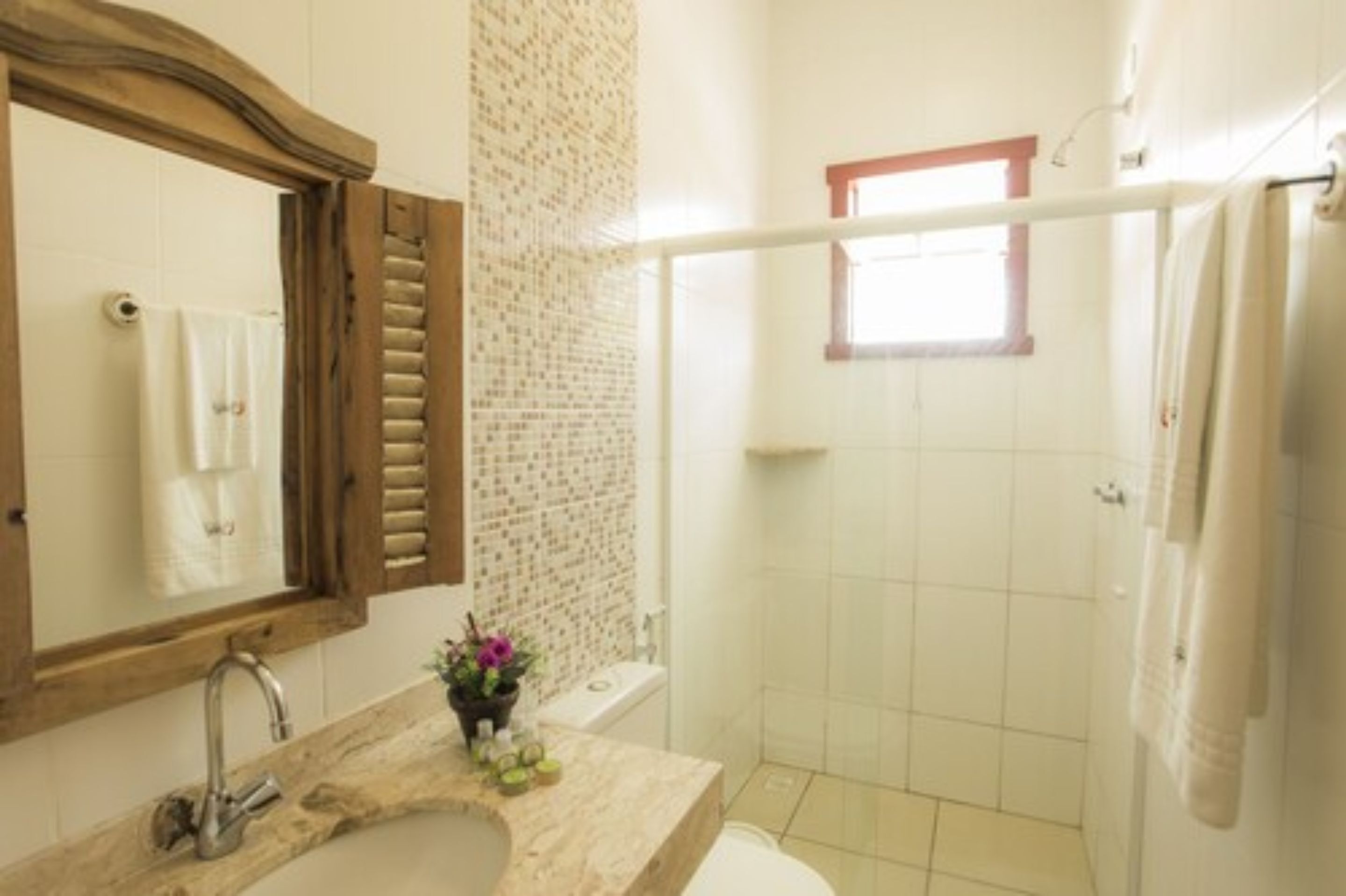 Een badkamer met een spiegel met houten lijst, een wastafel met een marmeren blad, een douchegedeelte en een raam dat natuurlijk licht binnenlaat.
