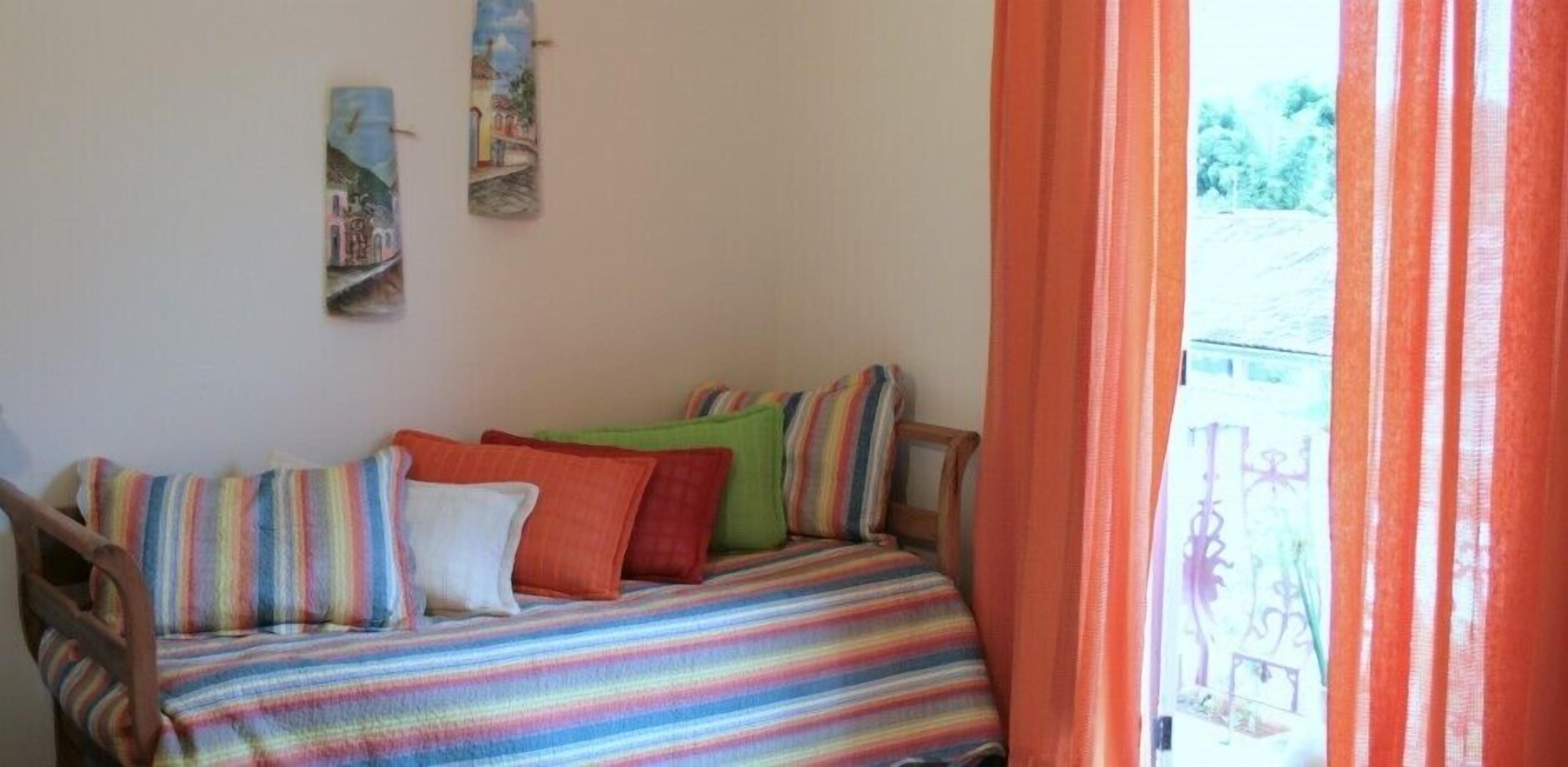 A room with a bed covered in a multicolored striped blanket, a wooden chair, and two wall-mounted paintings.