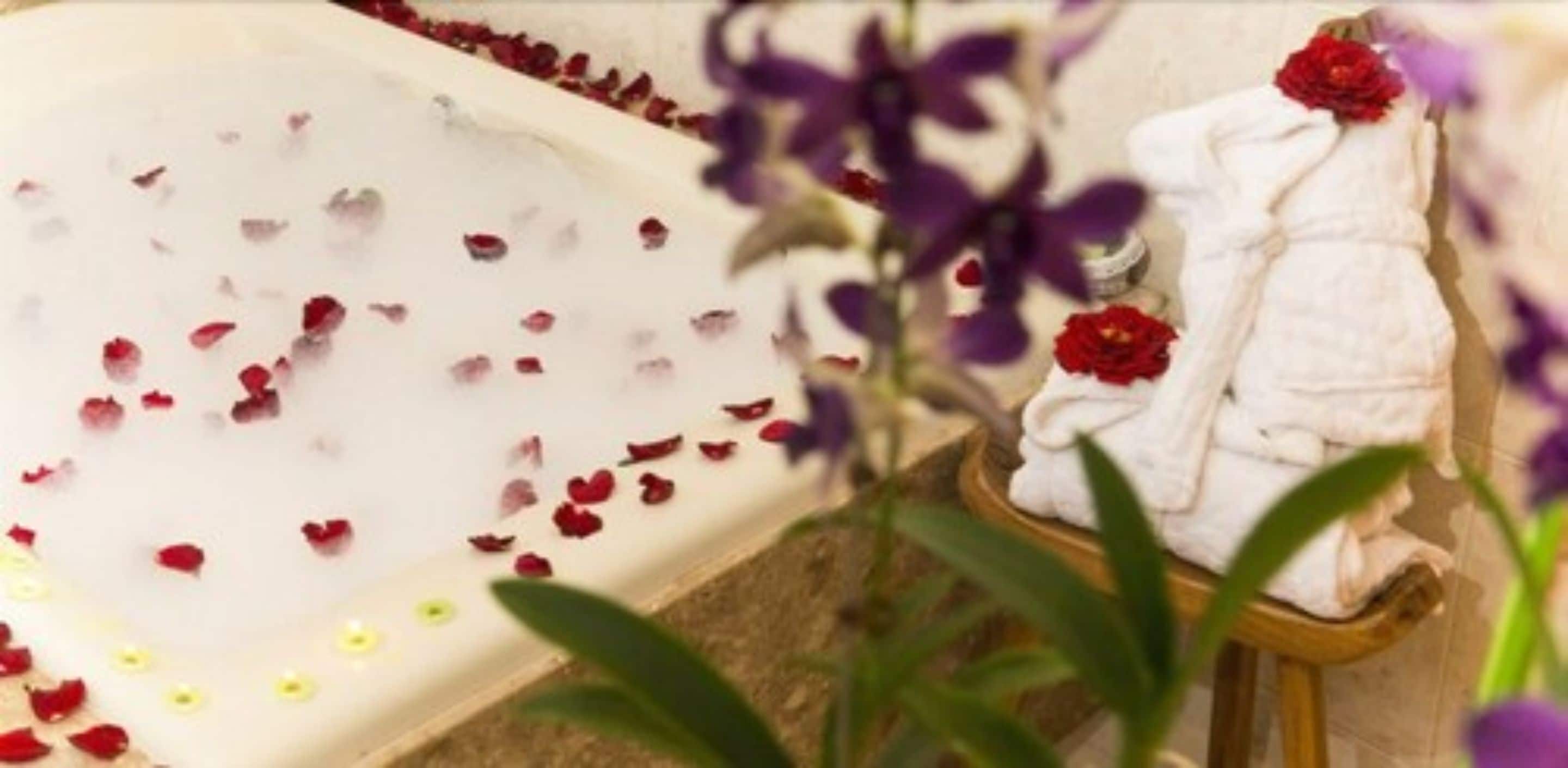 Una bañera con pétalos de rosa, una toalla y un arreglo floral.