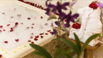 Una bañera con pétalos de rosa, una toalla y un arreglo floral.