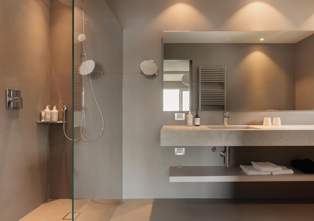 A modern bathroom with a glass shower enclosure, a large mirror, and a countertop with toiletries.