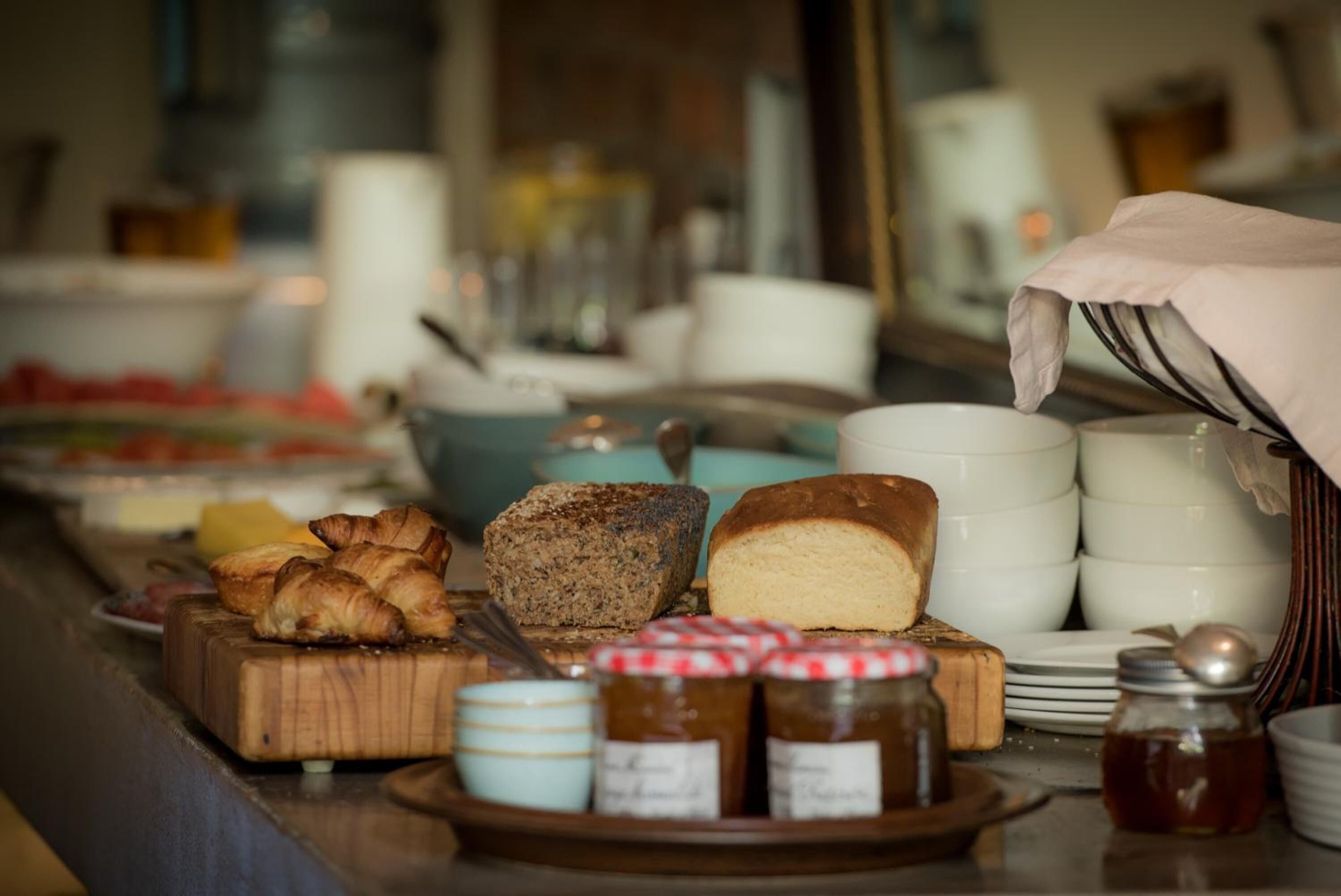 En morgenmadsbuffet med forskelligt brød og bagværk, blandt andet croissanter og et brød, samt syltetøj og honning.