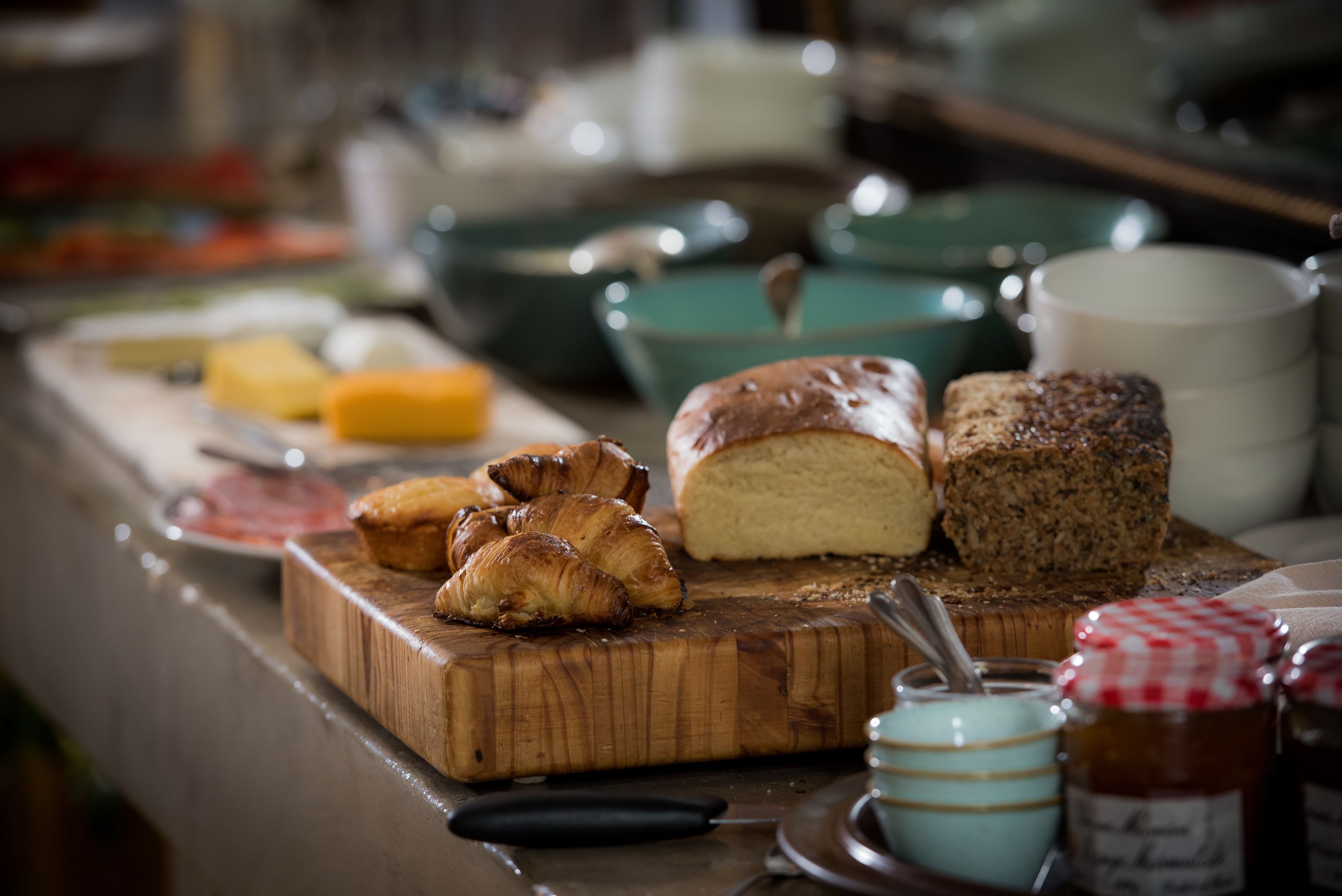 Una tabla de madera con pasteles y pan, un cuchillo y frascos de mermelada sobre una encimera de cocina.