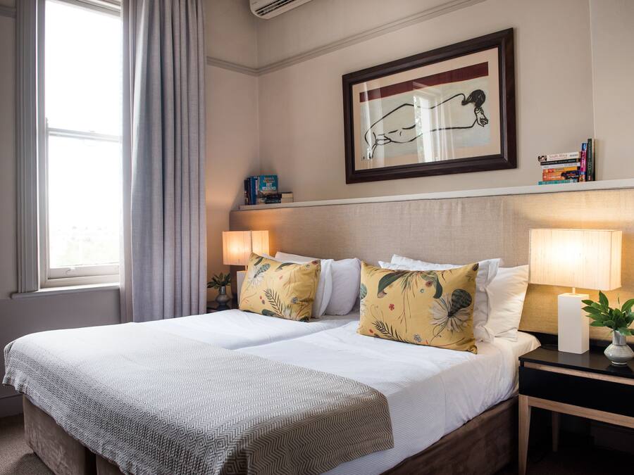 A hotel room with a large bed, two bedside tables, a framed artwork above the bed, and a window with curtains.