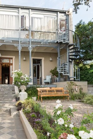 A two-story building with a spiral staircase, a wooden bench, and a garden with various plants and flowers. - Welgelegen House by RETURN Africa (Cape Town)