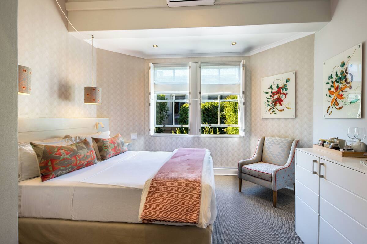 Un dormitorio moderno con una cama grande, una silla, un escritorio y un ventanal con vistas a zonas verdes.