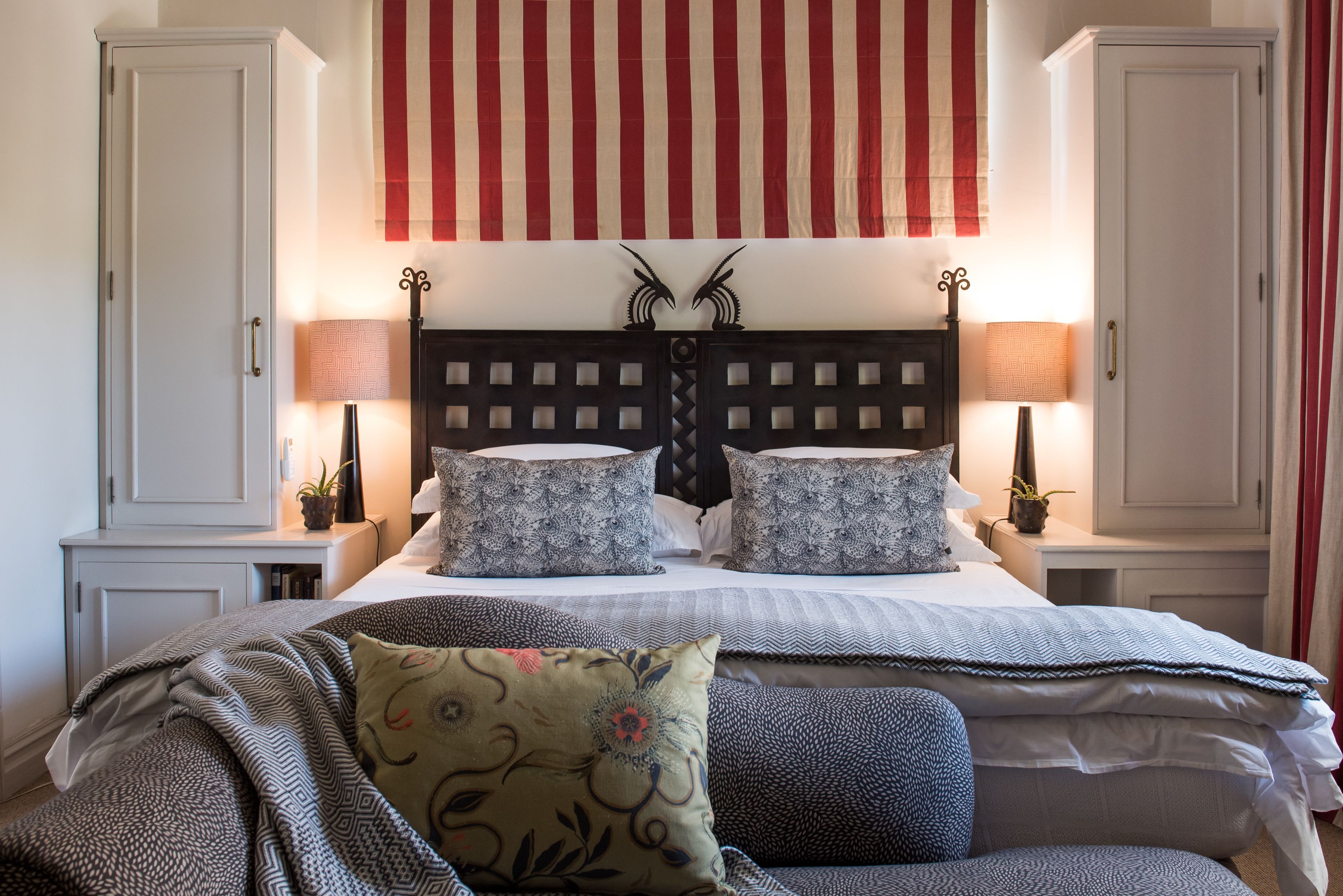 Un dormitorio ordenado con una cama, dos mesitas de noche, un cabecero decorativo y una gran bandera estadounidense.
