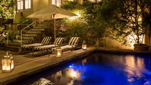 A poolside area with lounge chairs, a staircase, and a well-lit pool at night.