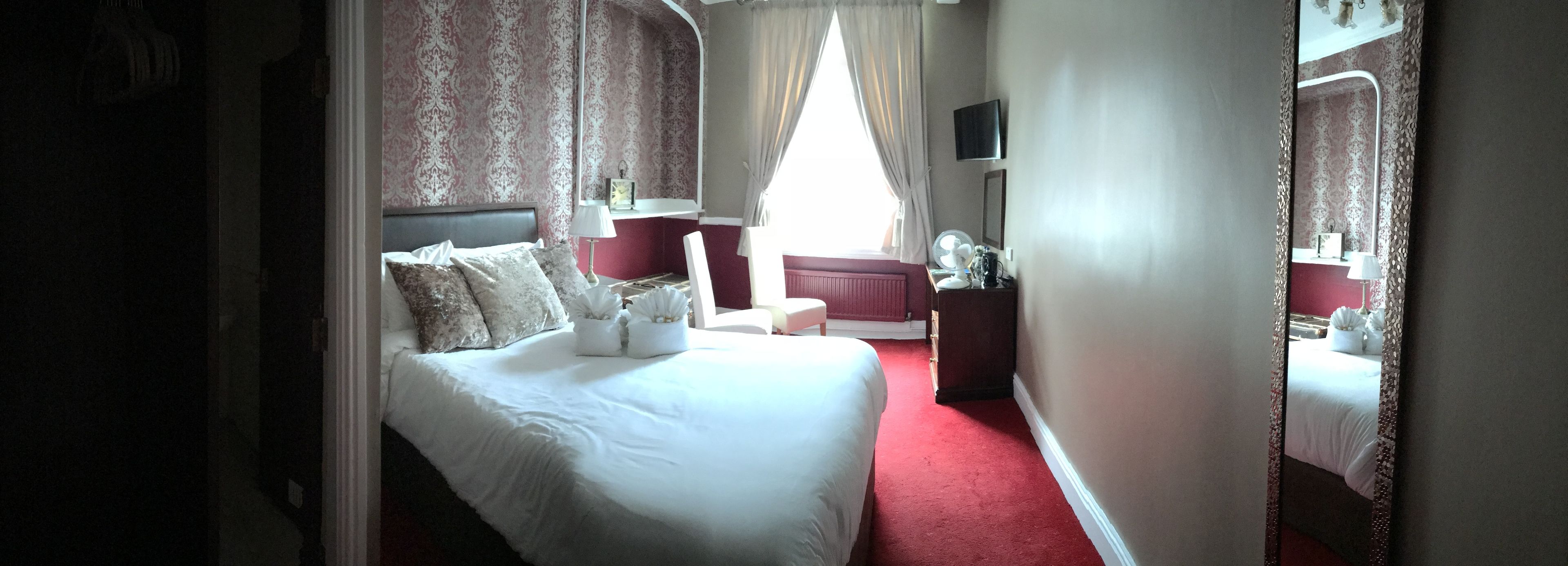 A hotel room with a large bed, a nightstand, a dresser, a mirror, and a television on the wall.