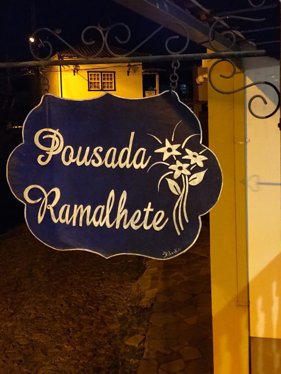 A sign with the name 'Pousada Ramalhete' in a decorative font, hanging above a doorway.