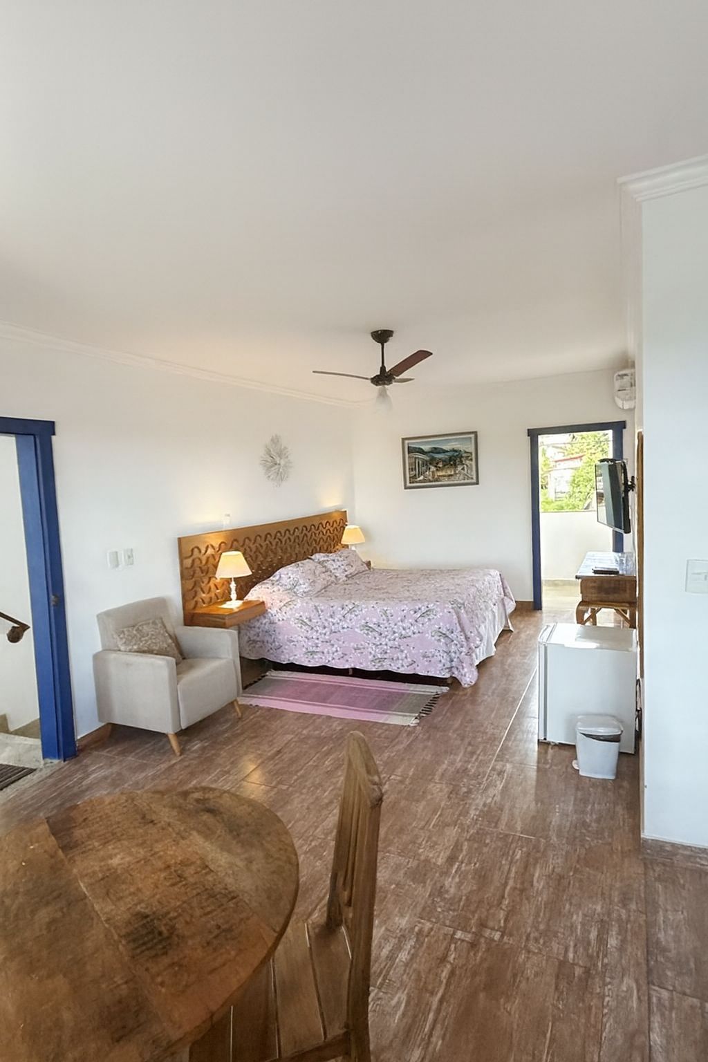 Un dormitorio con cama, una silla, una mesa, un ventilador de techo y una ventana.