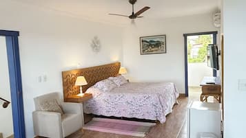 Un dormitorio con cama, una silla, una mesa, un ventilador de techo y una ventana.