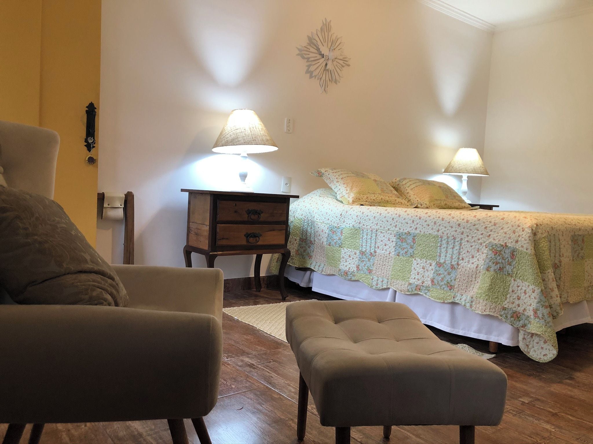 Un dormitorio con una cama, dos lámparas de noche, una mesita de noche, una silla y un reposapiés.