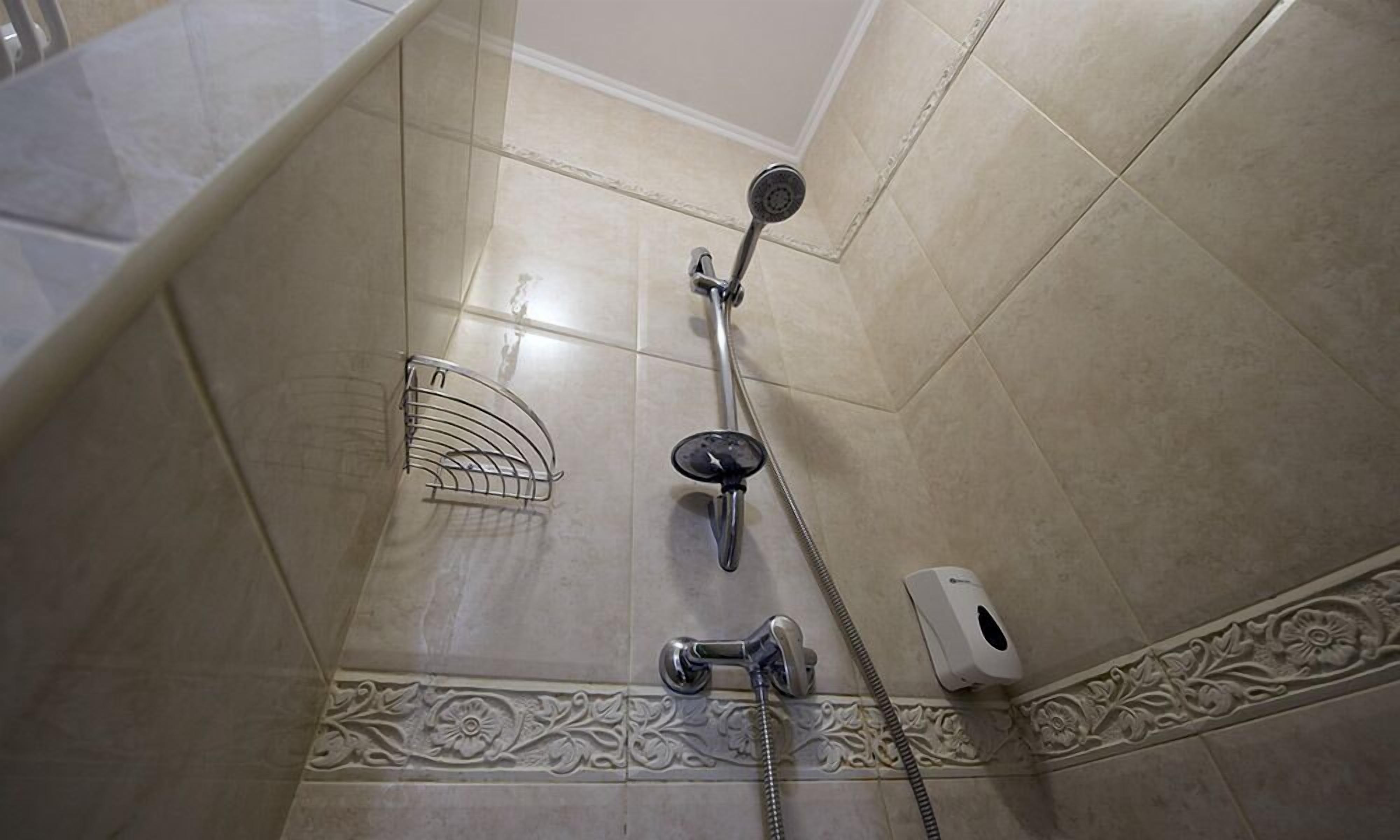 Canto de um banheiro com chuveiro, secador de mãos e um detalhe ornamental em azulejos.