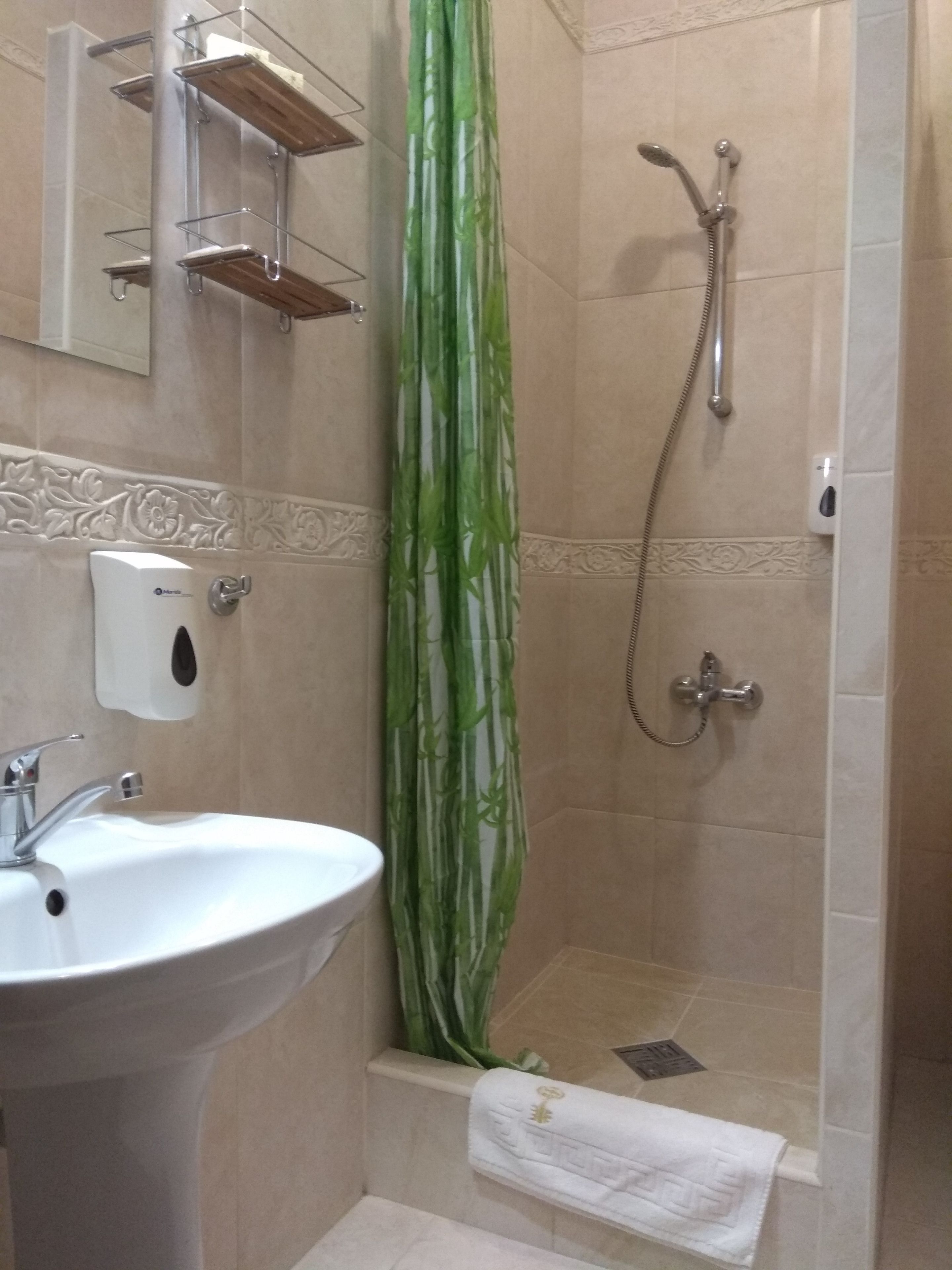 A bathroom with a white sink, a shower with a handheld showerhead, and a green shower curtain.