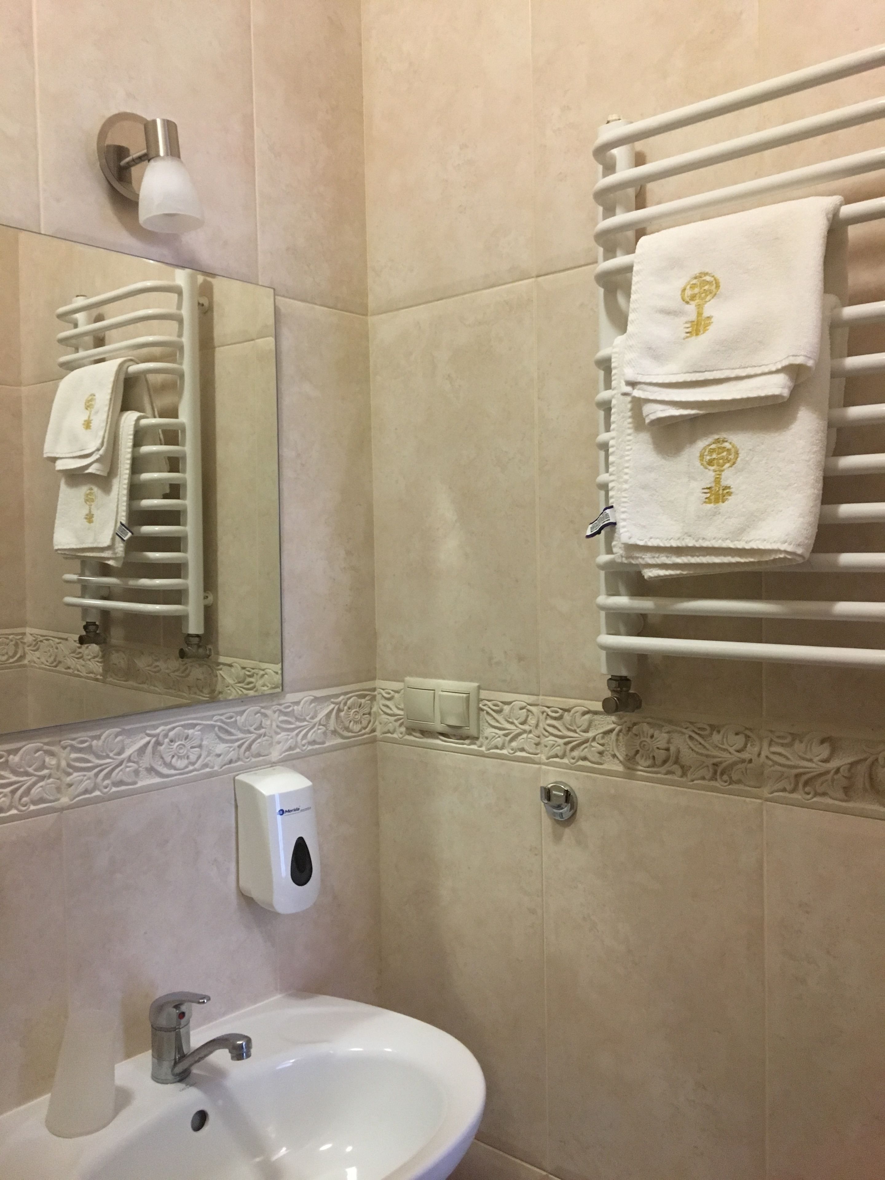 A bathroom with a sink, a towel rack with towels, a hand dryer, and a mirror.