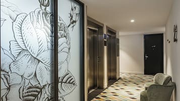 Un pasillo con piso estampado, una puerta corredera con diseño floral y dos ascensores.