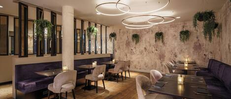 A modern restaurant with wooden flooring, dark sofas, and hanging plants.