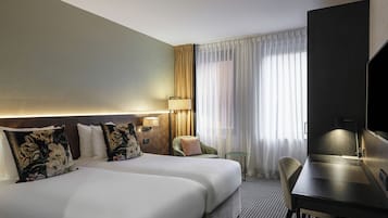 Habitación de hotel con dos camas, un escritorio, una silla, un televisor y un ventanal con cortinas.