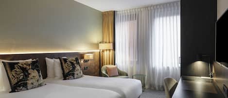 A hotel room with two beds, a desk, a chair, a TV, and a window with curtains.