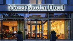 L’extérieur de l’hôtel Monet Garden se distingue par sa façade en verre, son entrée bien visible et son espace extérieur aménagé en coin salon.