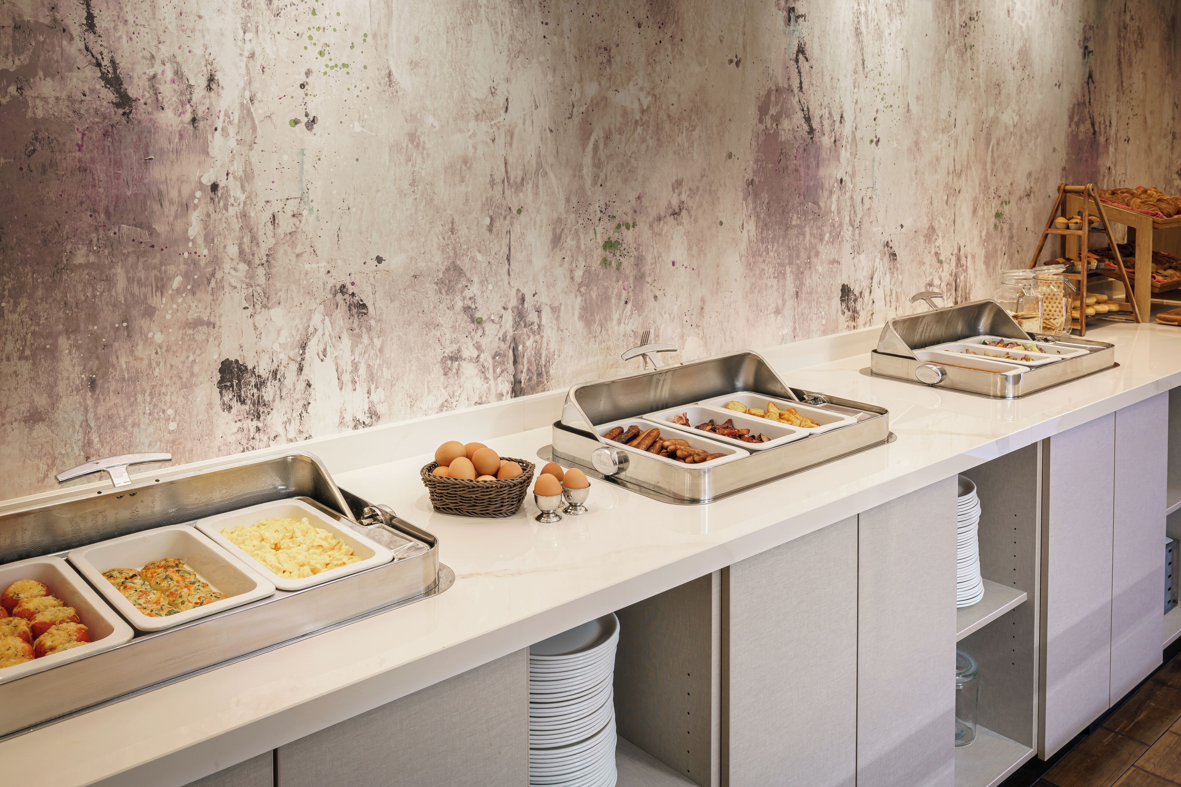 A buffet setup with various food items in trays, a basket of eggs, and a wooden display stand.