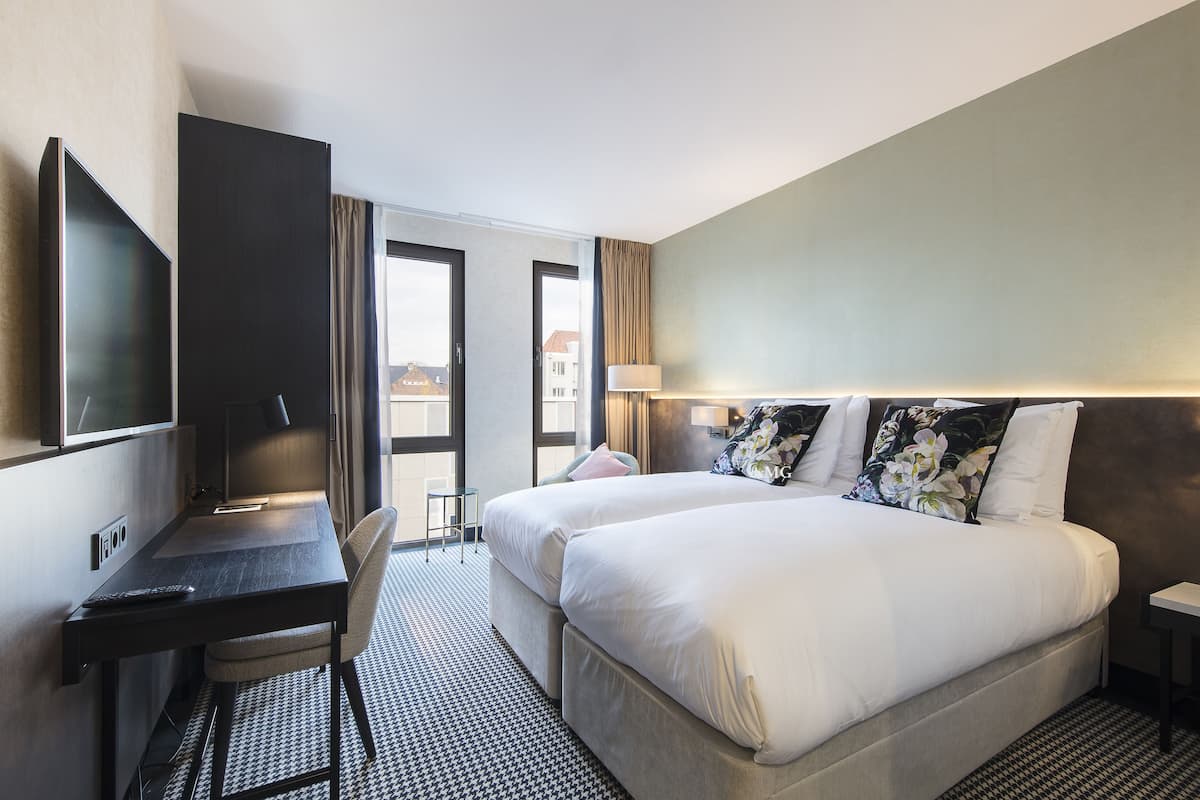 Ett hotellrum med två sängar, ett skrivbord, en stol, en TV och utsikt över staden.