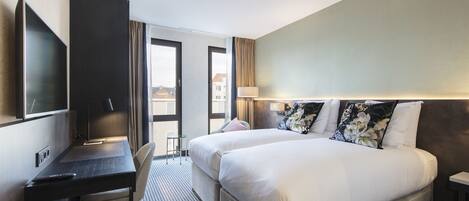 Habitación de hotel con dos camas, un escritorio, una silla, un televisor y vistas a la ciudad.