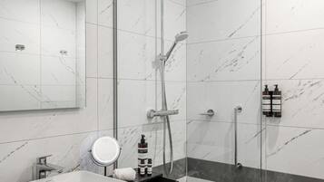 Een moderne badkamer met een glazen douchecabine, een wit wastafelmeubel en een wand betegeld met marmer.