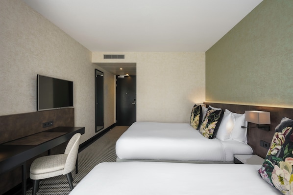 A hotel room with two beds, a desk, a chair, a TV, and a door leading to another room. - Monet Garden Hotel Amsterdam (Amsterdam)