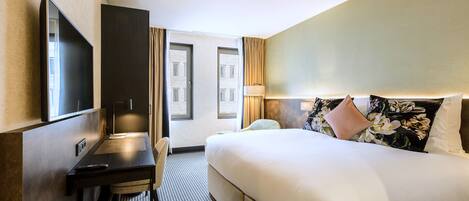 A hotel room with a bed, a desk, a chair, a television, and a window with curtains.