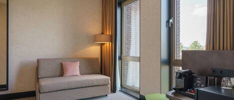 Une chambre d’hôtel avec un canapé, une lampe, une machine à café et une vue sur l’extérieur.