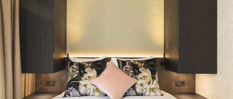 A neatly made bed with a floral pillow and a plain pillow, flanked by dark wooden nightstands with built-in lighting.