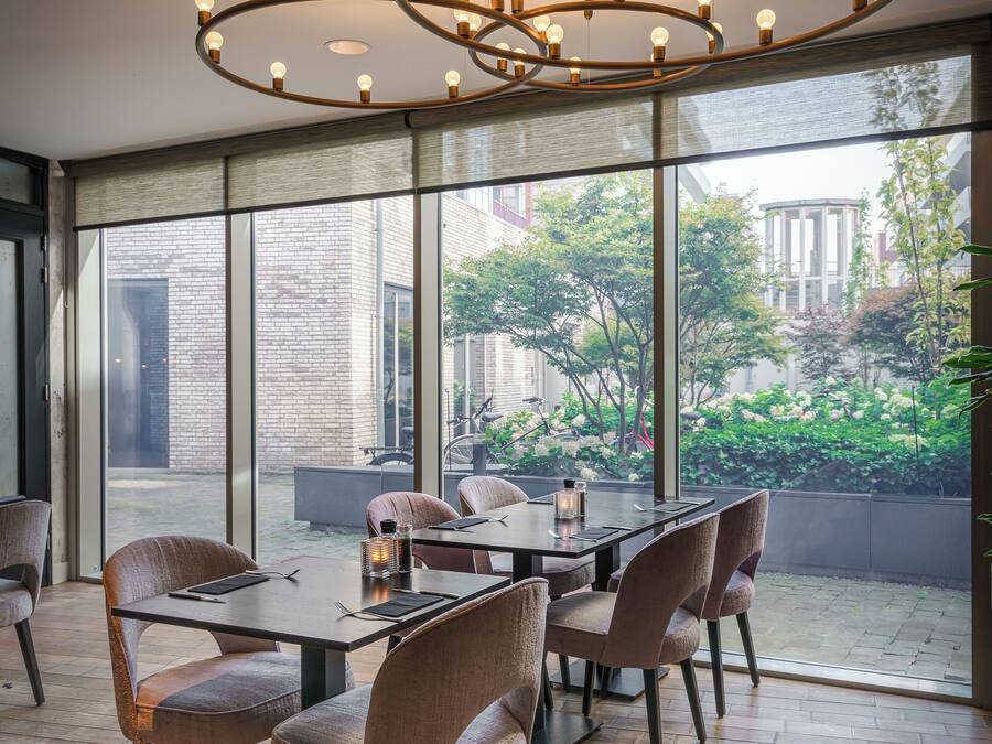 Un espace de repas moderne, doté d’une grande table et de chaises, d’un luminaire circulaire original et offrant une vue sur l’extérieur grâce à de grandes fenêtres.