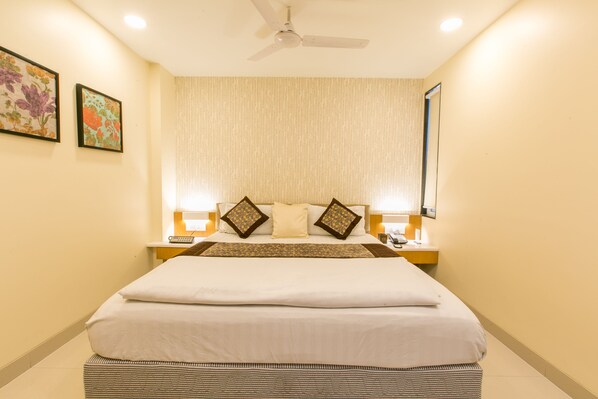 A hotel room with a large bed, two bedside tables, a ceiling fan, and two framed pictures on the wall. - Tulsi Casa (Bhopal)