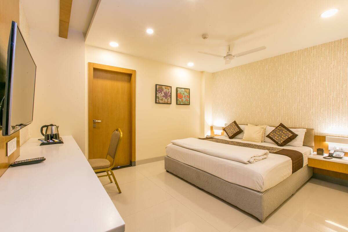 A hotel room with a bed, bedside table, TV, and a desk with a chair.