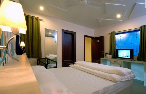A hotel room with a bed, a desk with a television, a chair, and a mirror. - Hotel Tulsi Exotic (Bhopal)
