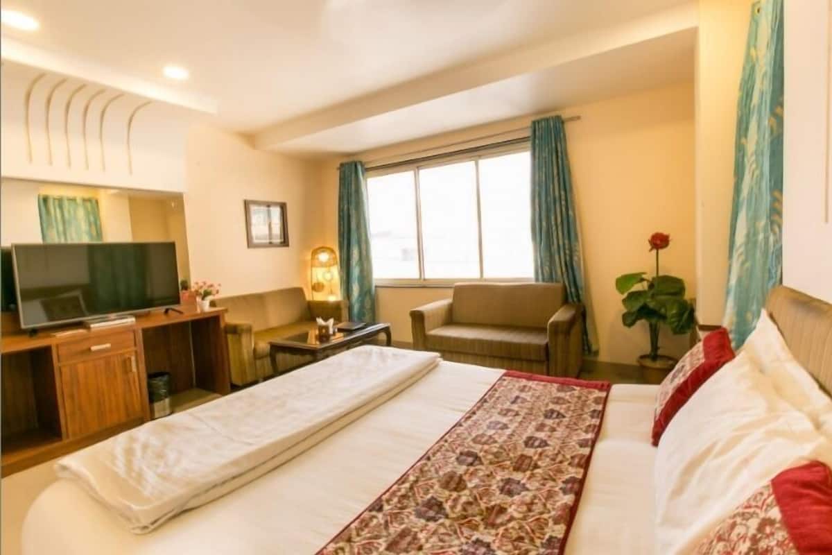 Habitación de hotel con cama, televisor, escritorio, silla y ventana con cortinas.