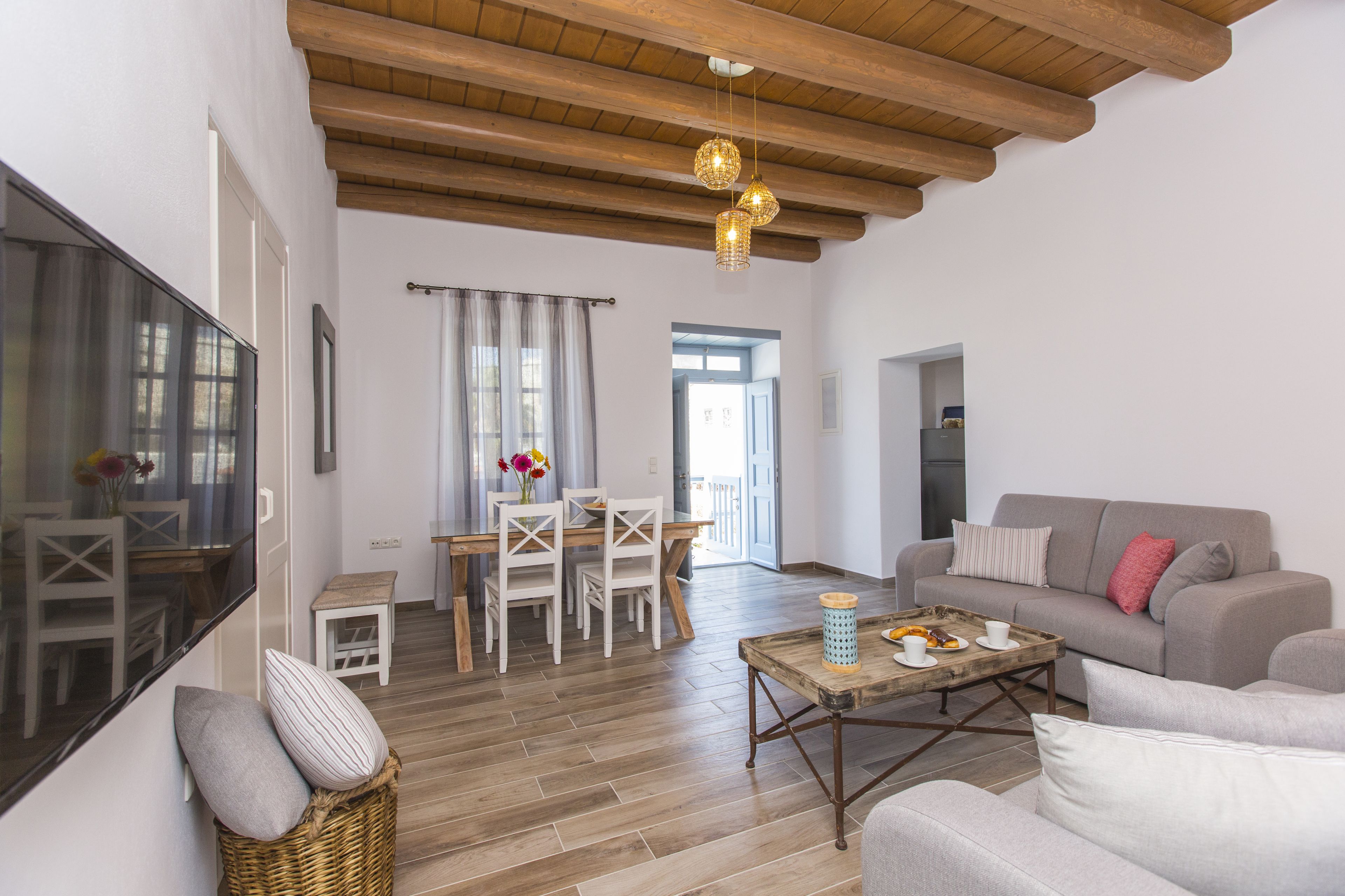 Una sala de estar moderna con techo de madera, un sofá gris, una mesa de centro de madera y un comedor con una mesa y sillas blancas.